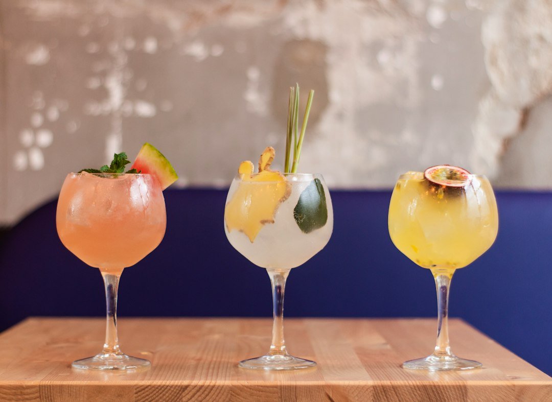 A tall glass mocktail garnished with cucumber ribbon, fresh mint, and lemon slices on a wooden table in a sunny New Zealand garden setting